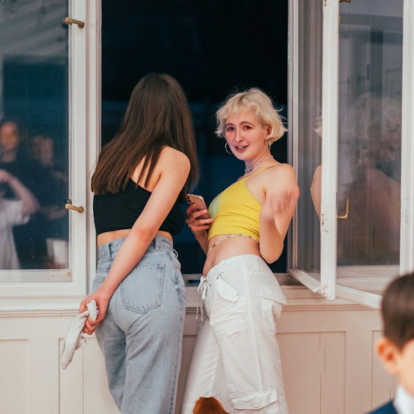 two women standing on a window sill looking at a cell phone