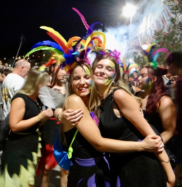 Two women with colorful feathered headdresses hugging